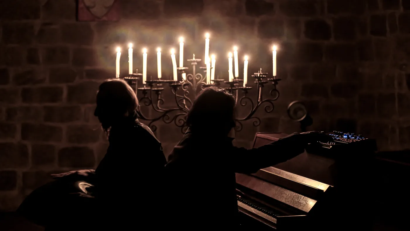 Silhouette al pianoforte nella luce di un candelabro, dietro un muro in mattoni