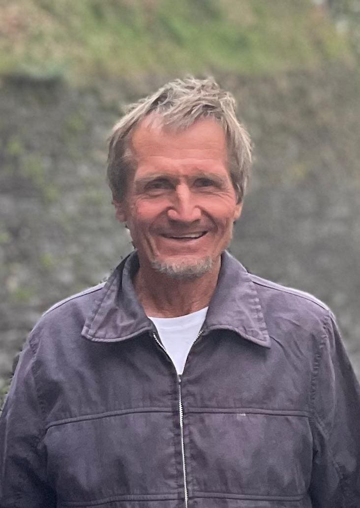 Portrait of Ernst Götsch in 2022, smiling, outdoors in front of a stone wall.