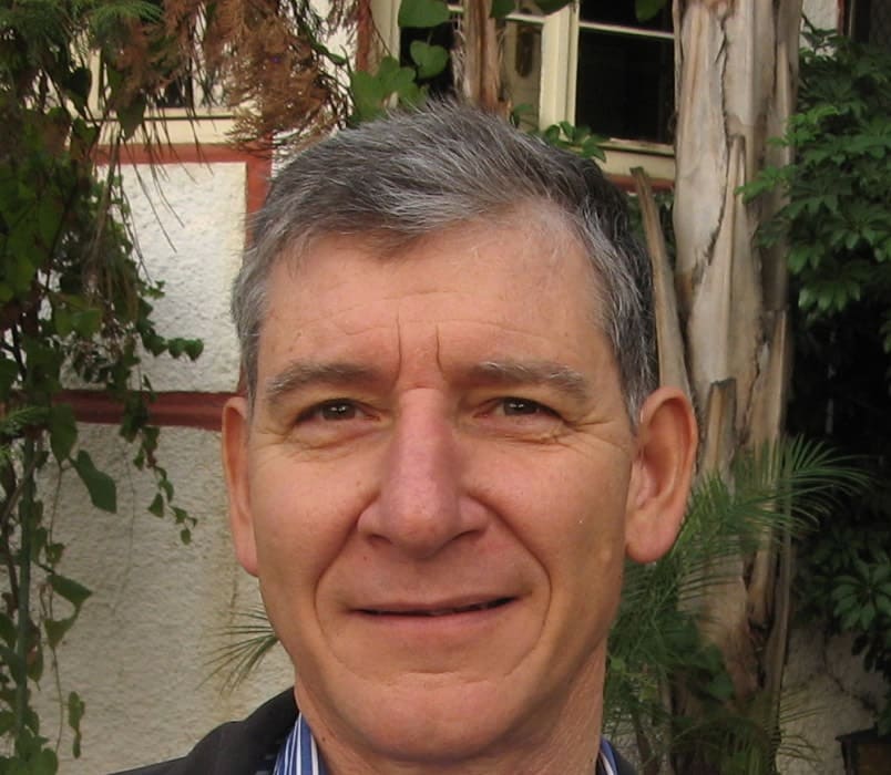 Head-and-shoulders portrait of Tony Rinaudo outdoors in front of a building with plants.